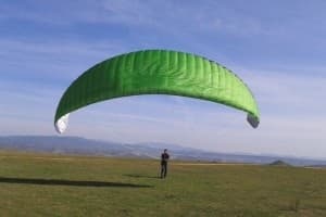 Green paraglider wing inflated over grassy launch field in Spain