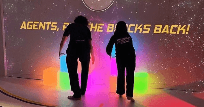 Participants interacting with illuminated cubes before a projection wall