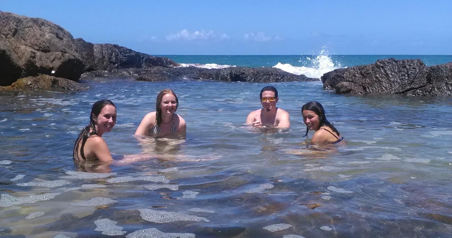 Swimmers relaxing in rocky tidal pool at sunny coastal beach