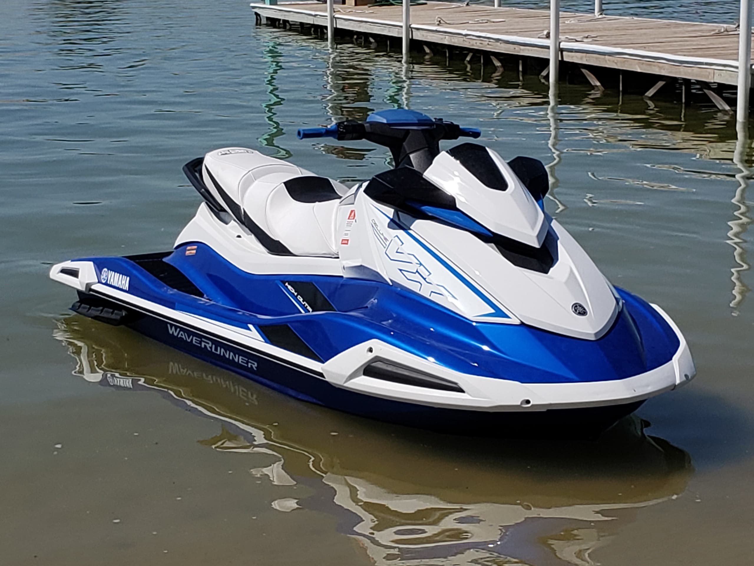 Blue and white jet ski tied at marina on clear shallow lake water