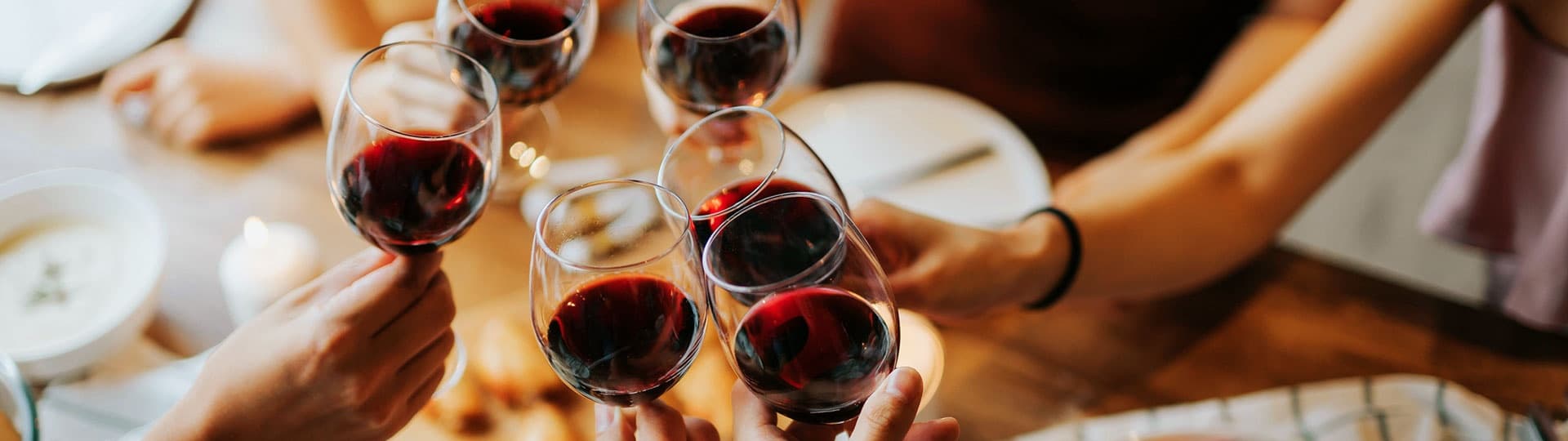 Friends toasting red wine at rustic pasta shop communal table