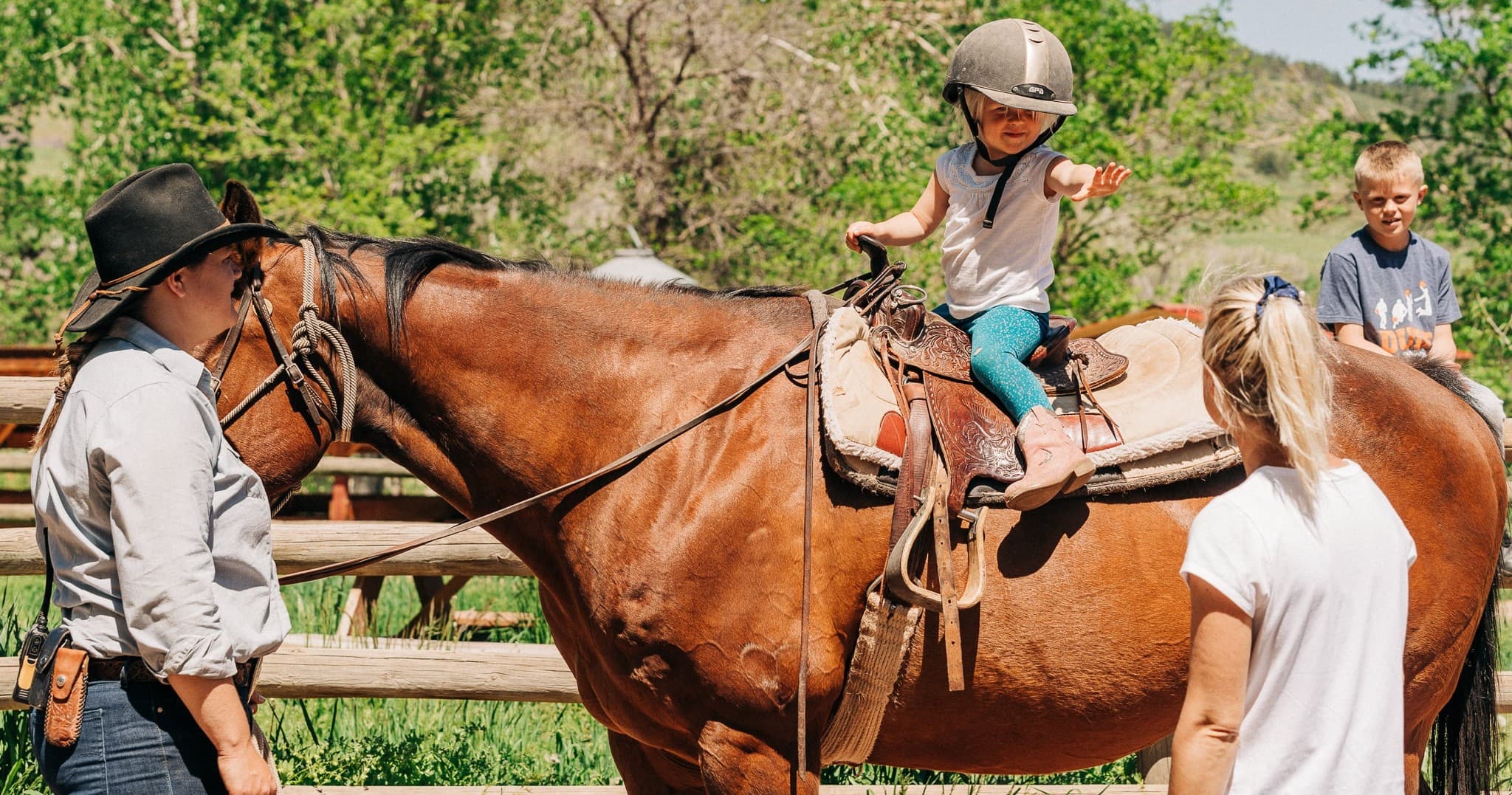 Child learning to ride on ranch horse with guide nearby