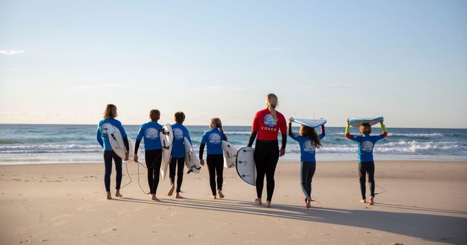 Surfers walking on sandy beach toward ocean at sunrise