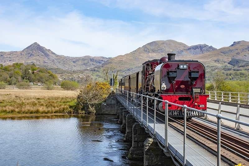 Heritage train crossing narrow bridge over reflective river