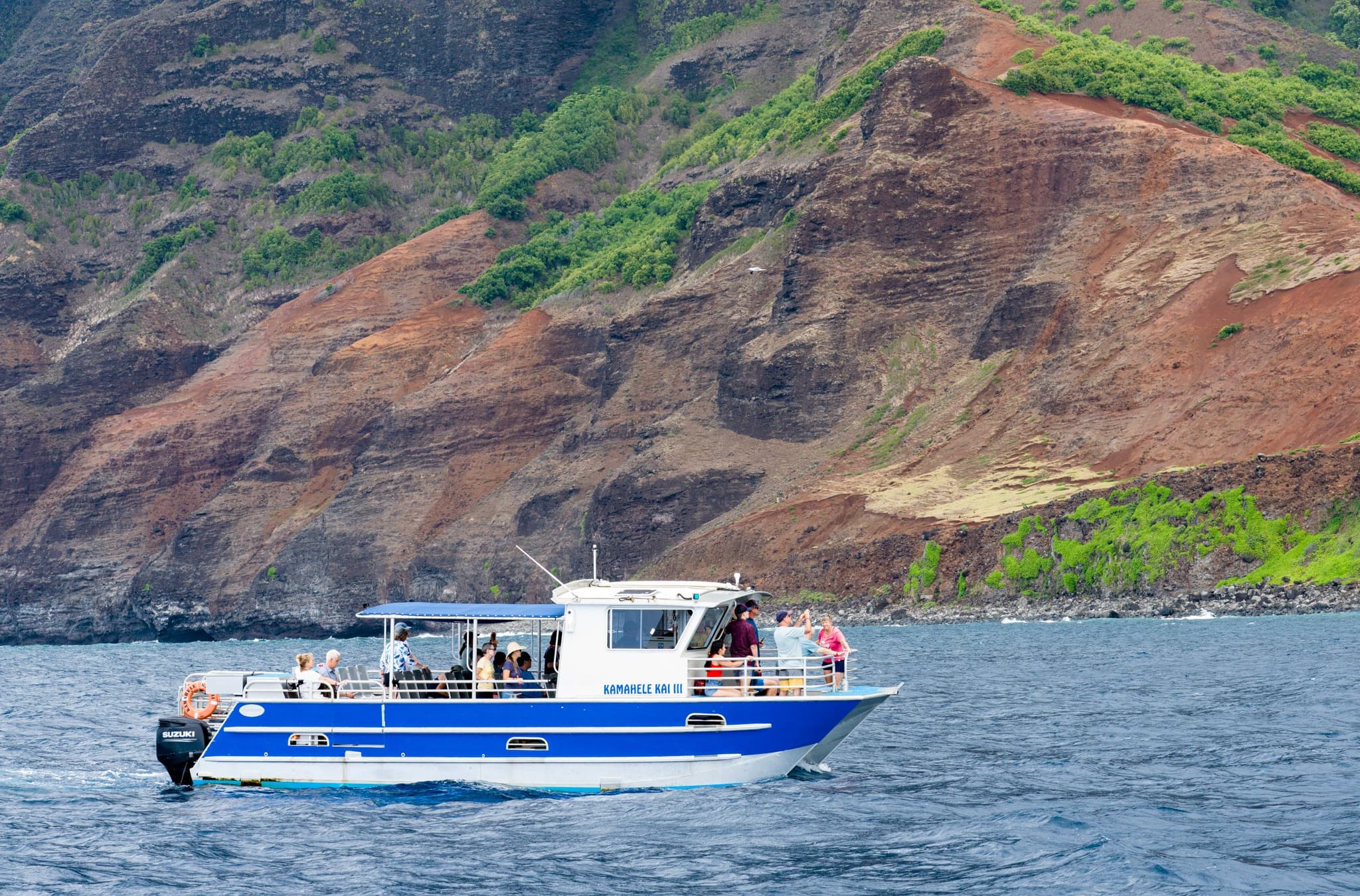 Catamaran tour cruising past vibrant Na Pali Coast cliffs, Kauai
