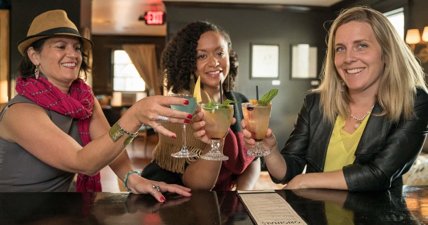 Friends toasting cocktails at bar during social food tour night