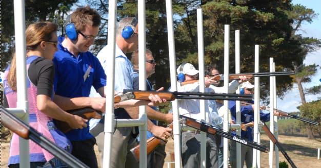 Line of clay shooters firing from bays on sunny outdoor range