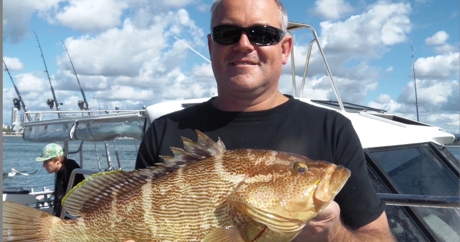 Angler posing with big reef fish under blue sky at sea
