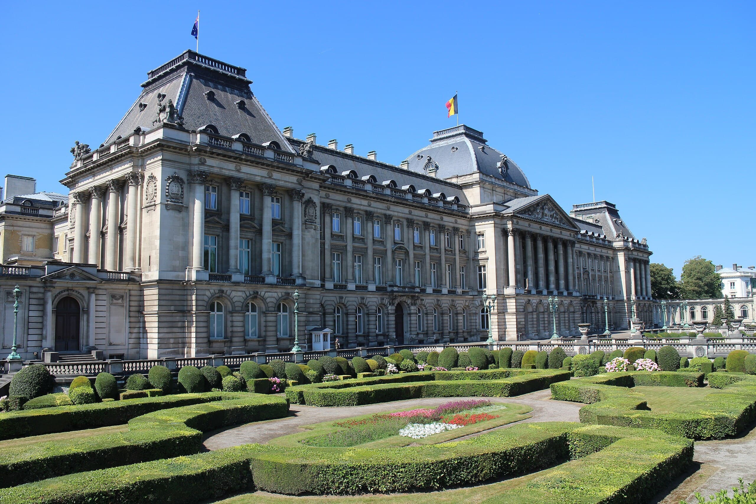 Grand palace with formal gardens and manicured hedges under blue sky