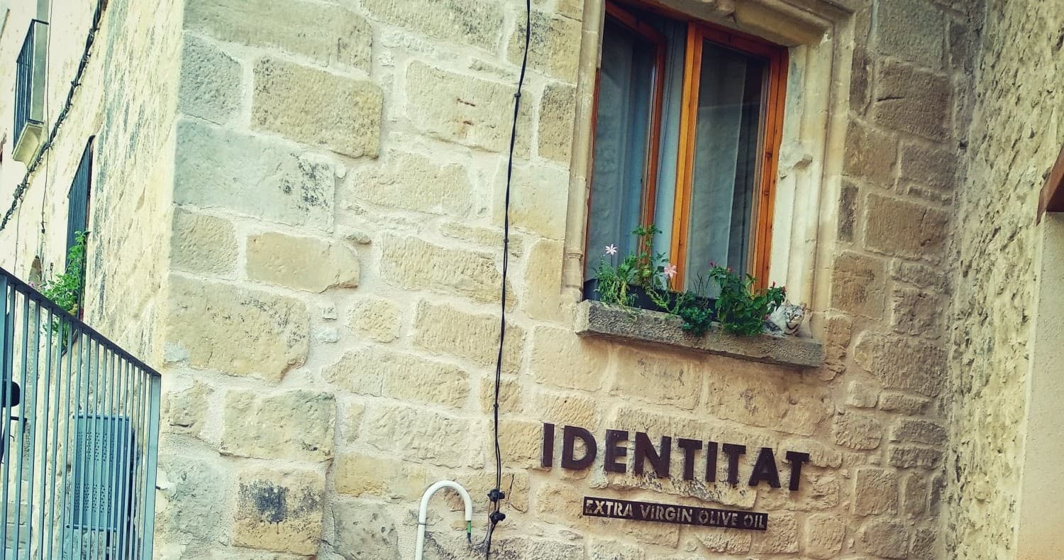 Stone farmhouse facade with IDENTITAT sign in village setting