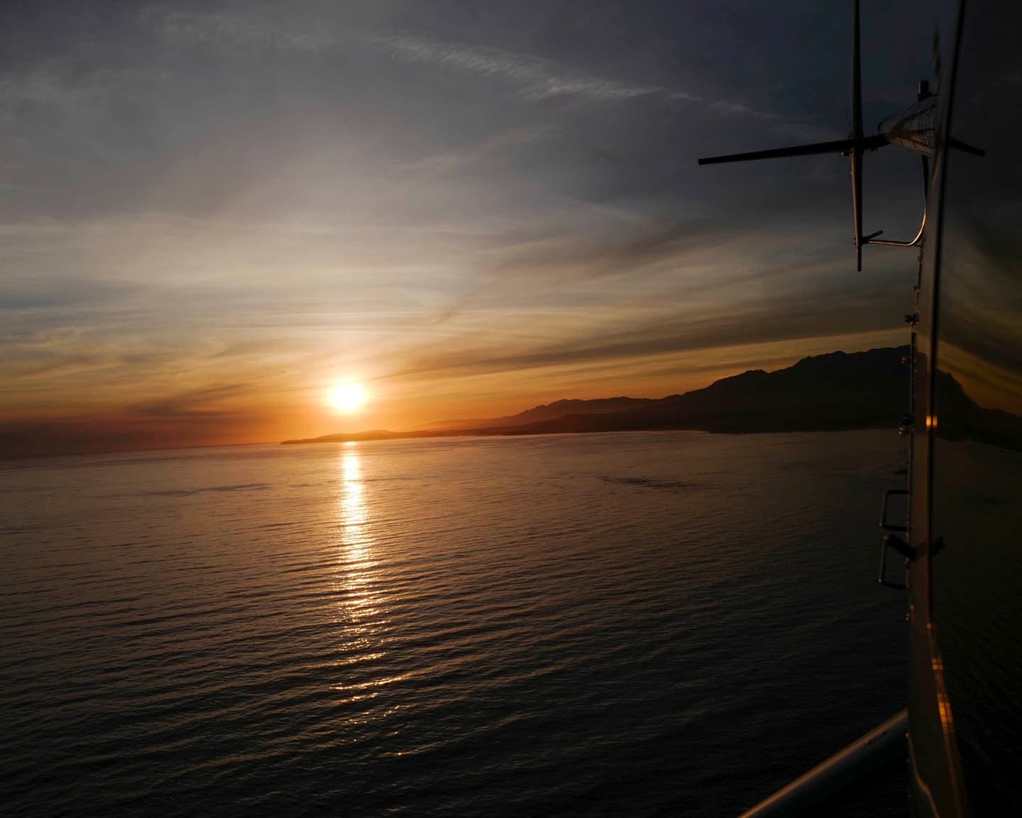 Sunset over ocean seen from helicopter deck during coastal tour
