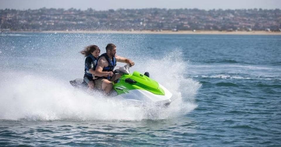 Two riders on green jet ski speeding across coastal waters