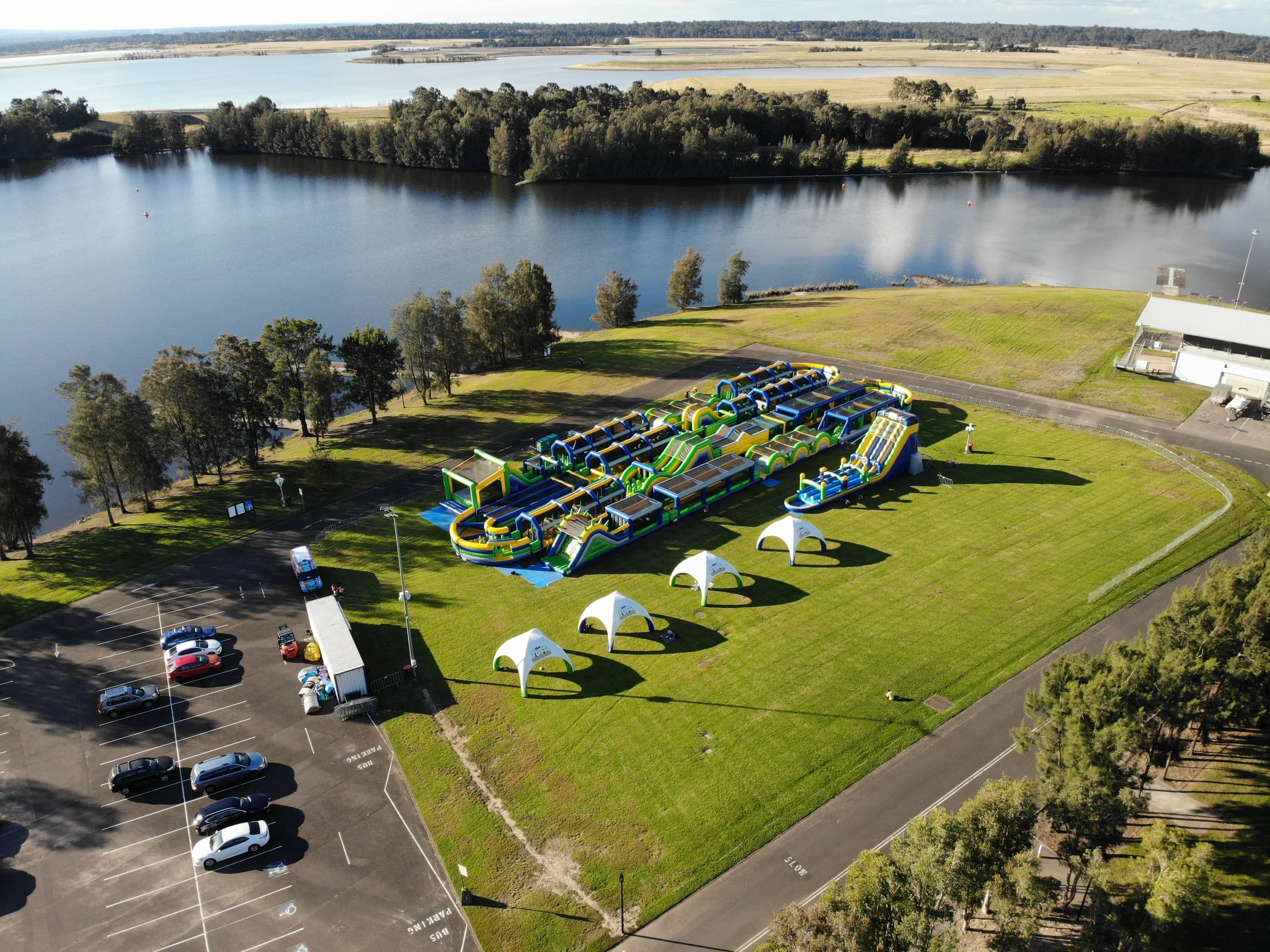 Large inflatable obstacle course beside river with parking area
