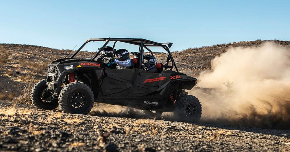 UTV tearing through dusty desert trail under wide blue sky