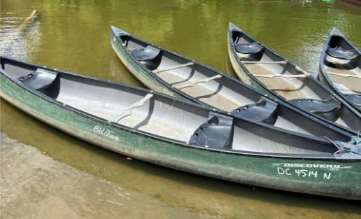 Stacked canoes resting in shallow river, rental boats ready