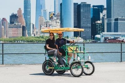 Couple riding four-person surrey bike along Manhattan waterfront