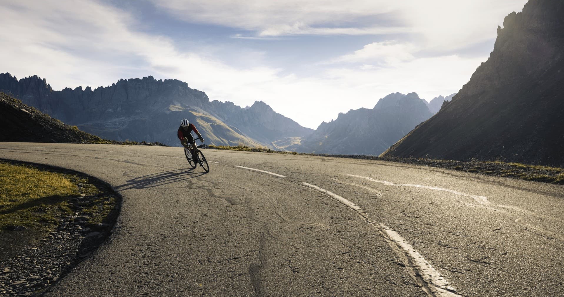 Solo cyclist riding empty mountain road under alpine peaks