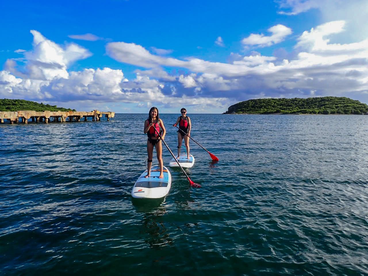 Two paddleboarders gliding on calm tropical bay under blue sky