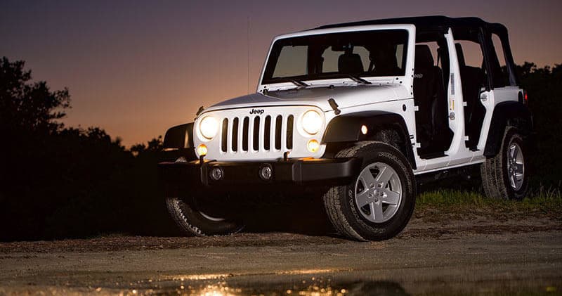 White Jeep off-road at dusk on trail with illuminated headlights