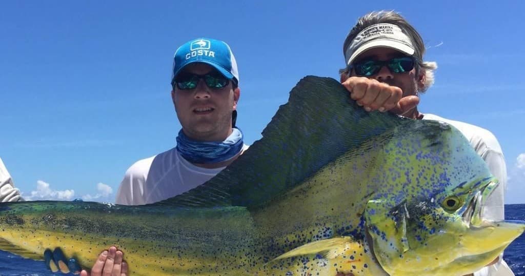 Anglers holding large mahi-mahi on deck with blue sky and sea