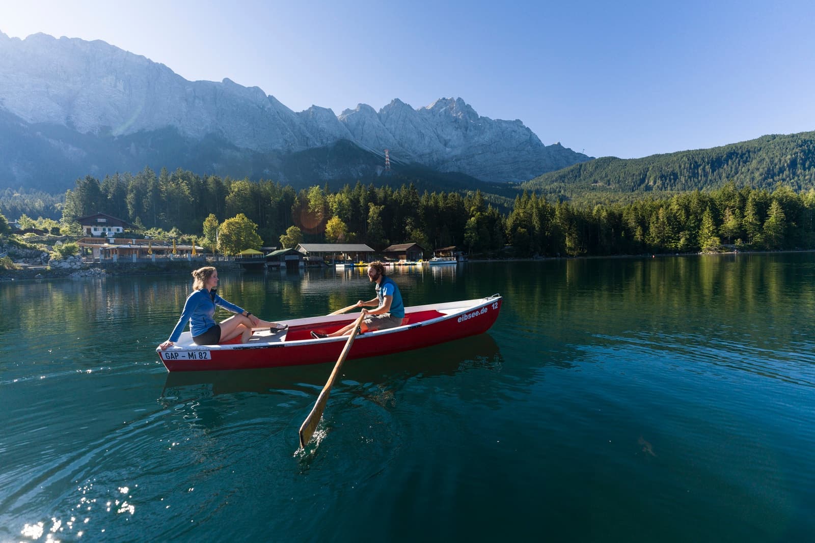 Two people rowing a red boat on crystal Eibsee waters