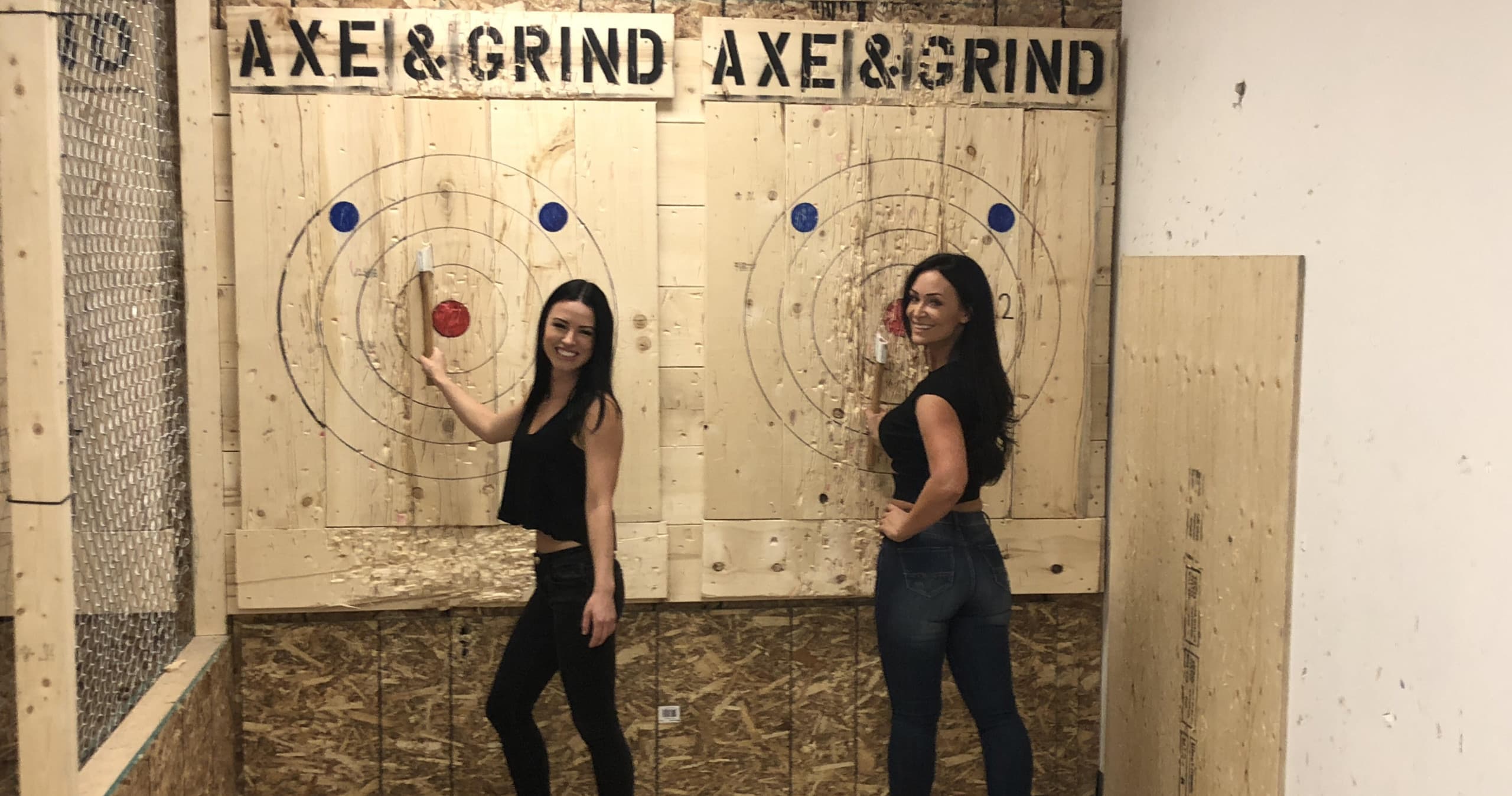 Two women smiling in indoor axe-throwing lane with targets