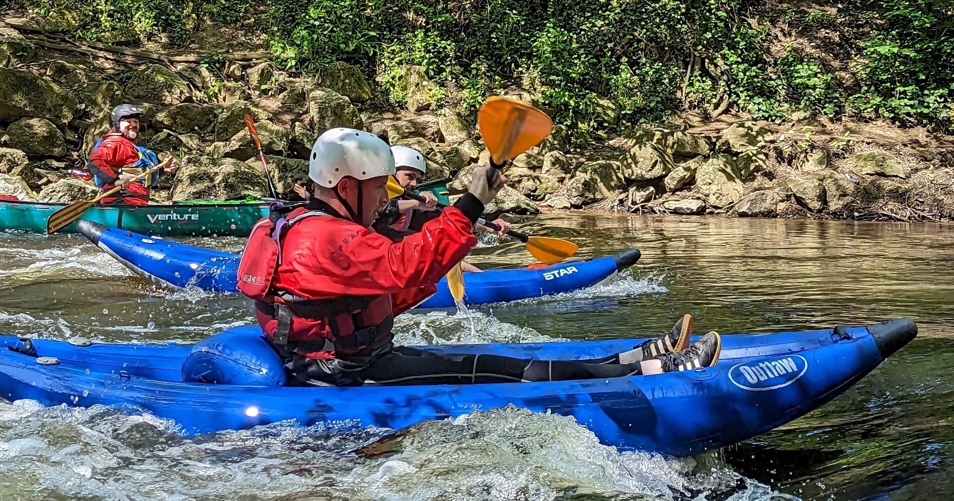 Kayaker paddling blue kayak through river rapids with spray