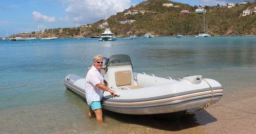 Man launching inflatable dinghy from sandy beach into calm bay