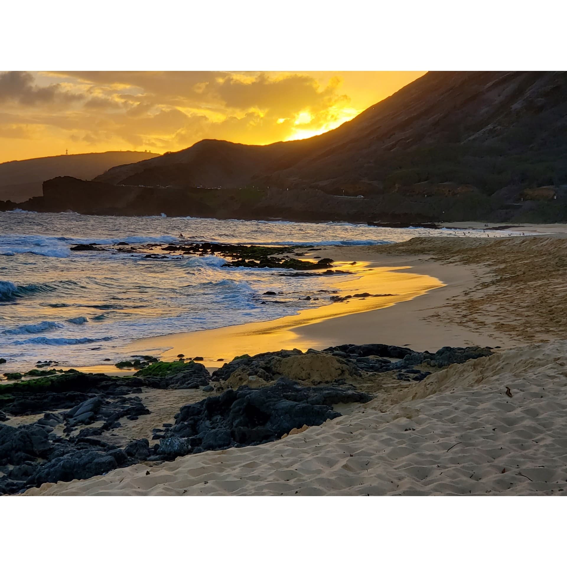 Rocky shoreline with golden sunset reflecting on beach