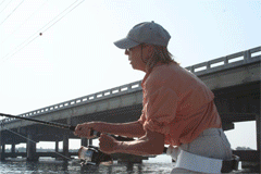 Fisher casting line from boat under highway bridge at sunrise