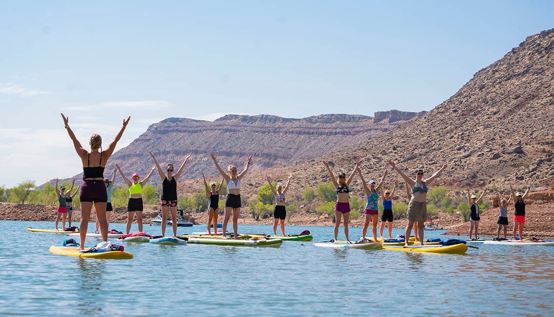 Large group paddleboarding on scenic lake with cliffs