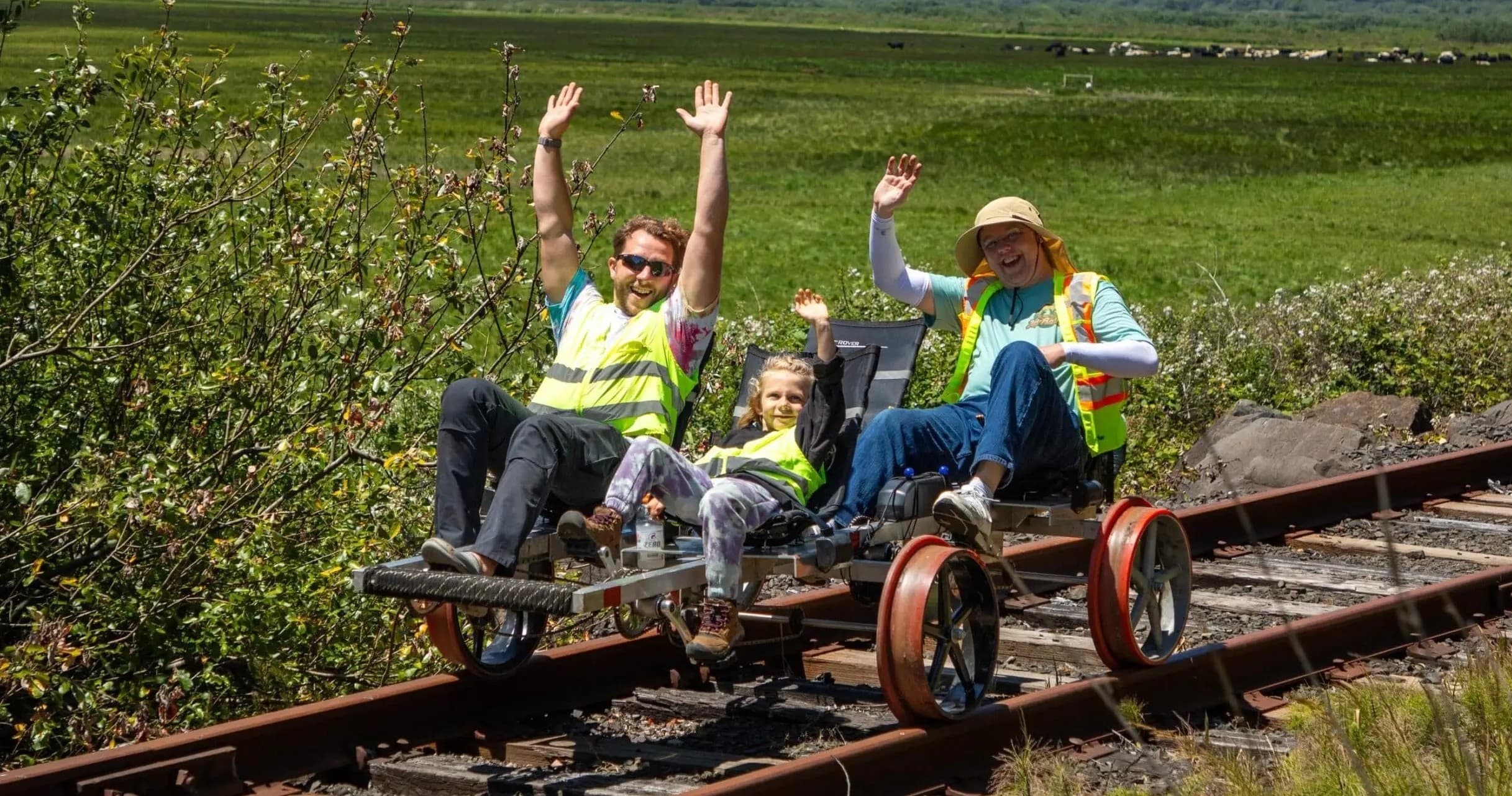 Family rail-bike riding across scenic marshland tracks waving