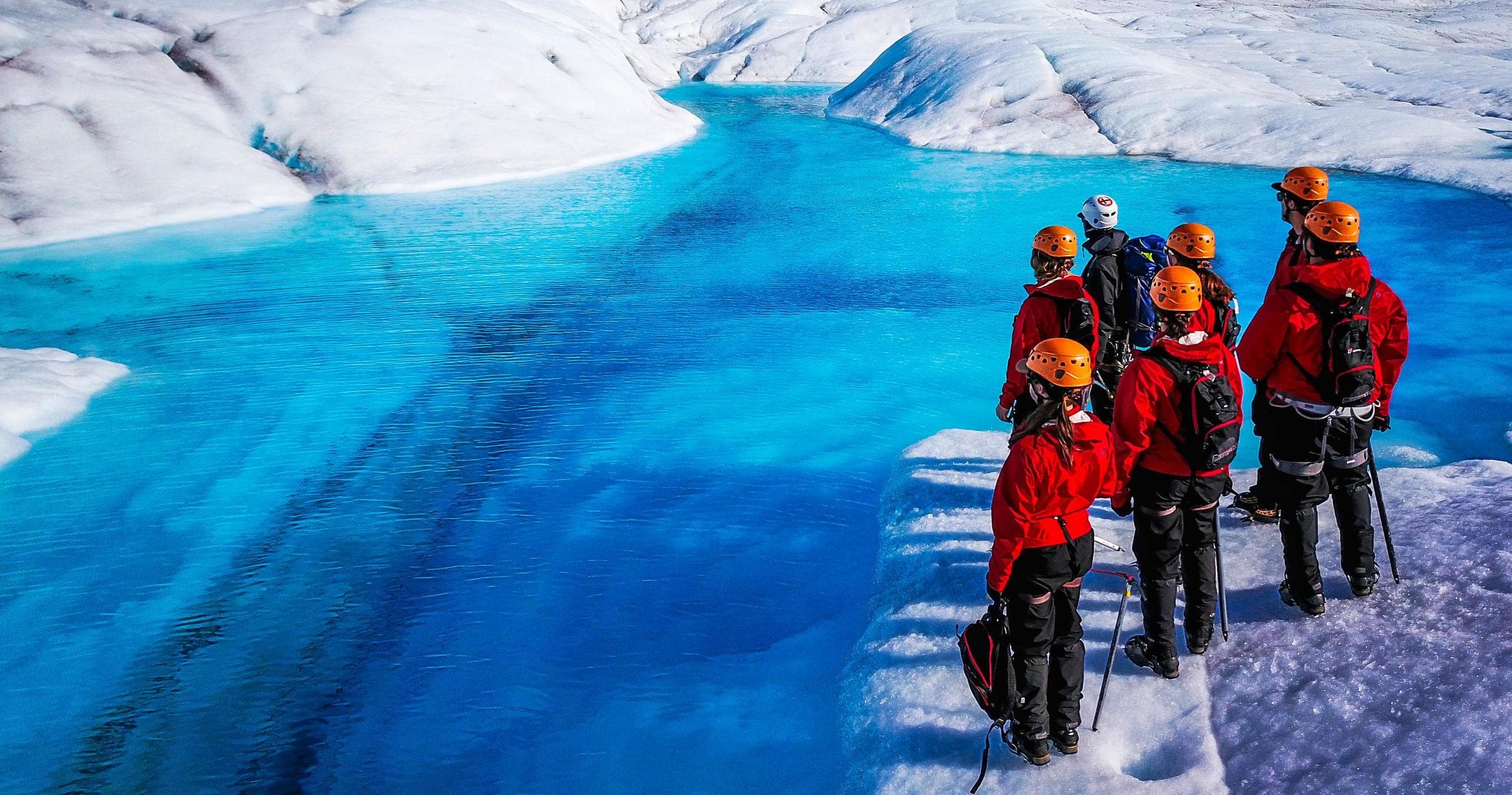 Guided glacier trek beside vivid blue ice meltwater in Alaska
