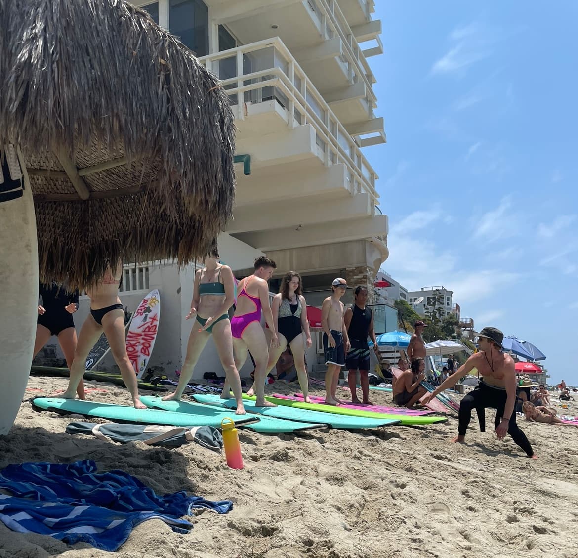 Group surf lesson on crowded sandy beach with surfboards