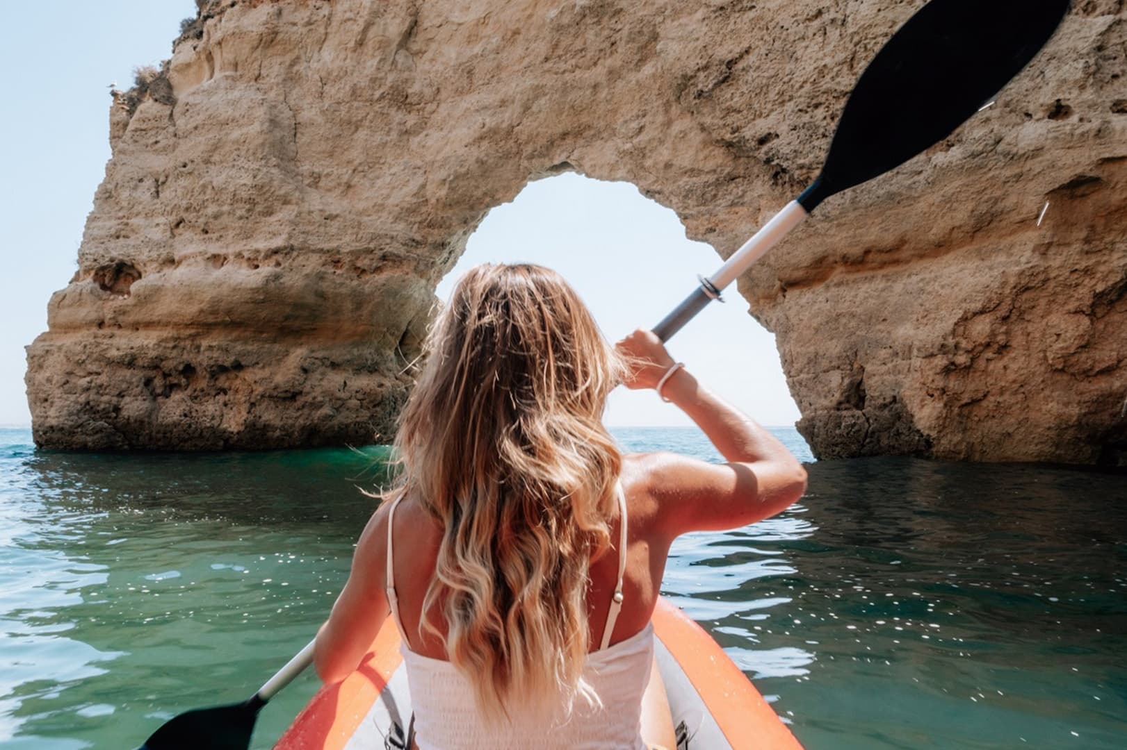 Solo kayaker paddling through coastal sea arch formation