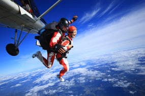 Skydivers exiting plane with dramatic cloudscape and ocean below