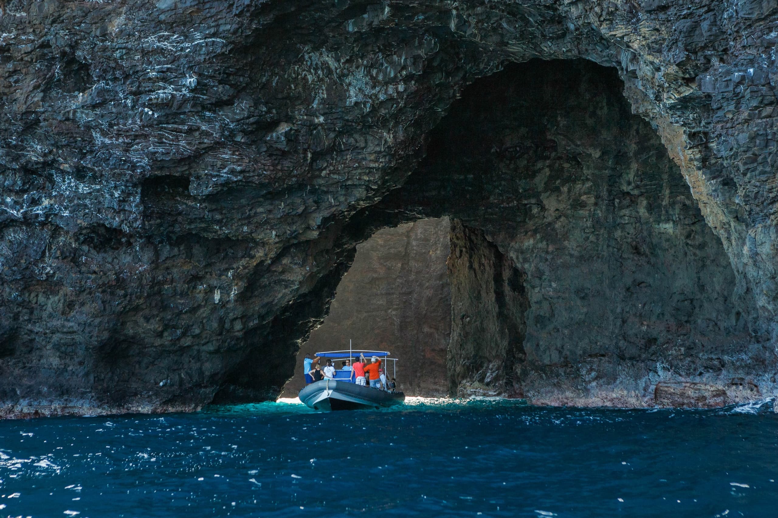 Small tour boat entering dramatic sea cave arch along coast