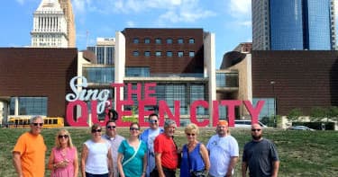 Tour group posing by 'The Queen City' sign with city skyline