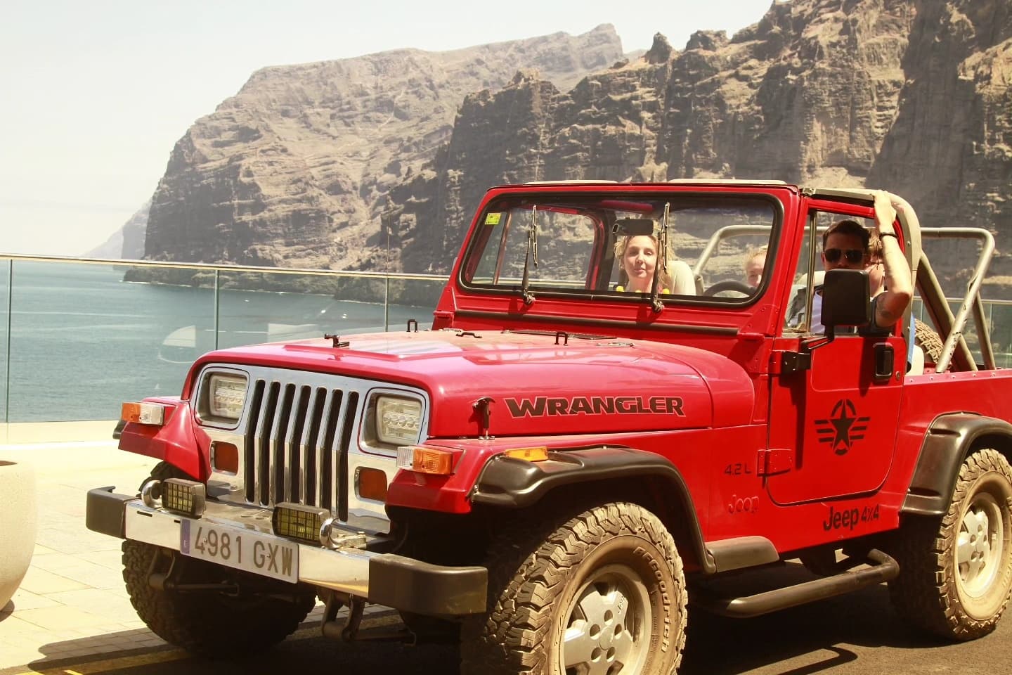 Red Jeep driving beside coastal cliffs on scenic ocean overlook