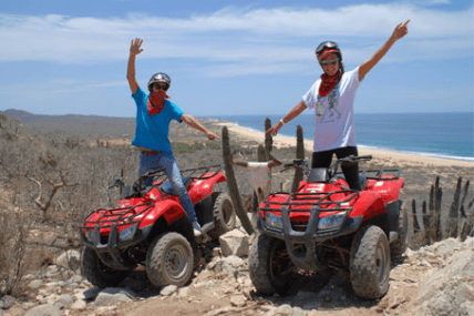 Two riders on red ATVs on coastal desert trail overlooking ocean