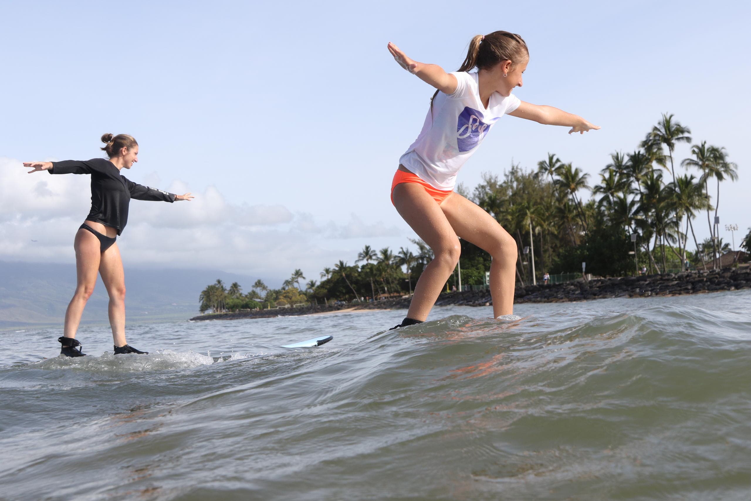Young surfers carving gentle wave with palm-lined Maui coastline