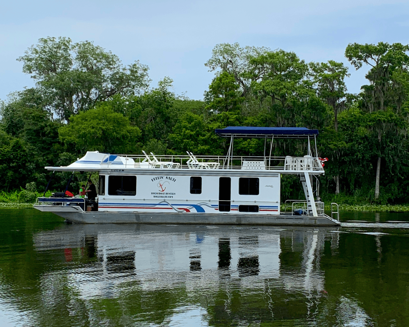Spacious houseboat reflected on still river near wooded shore
