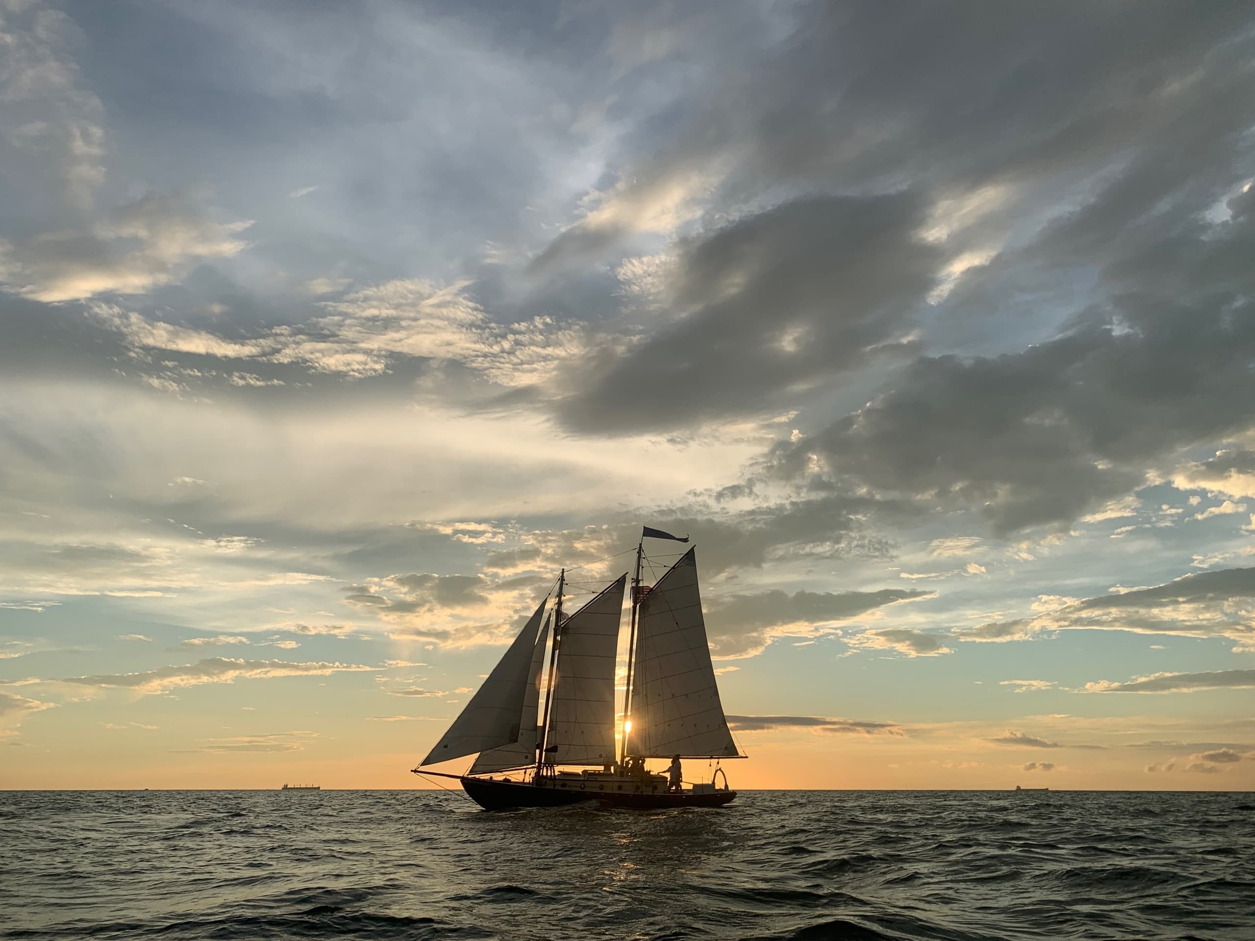 Schooner sailing at sunset on open sea with dramatic clouds