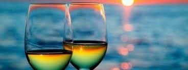 Two wine glasses by ocean at sunset for romantic waterfront evening