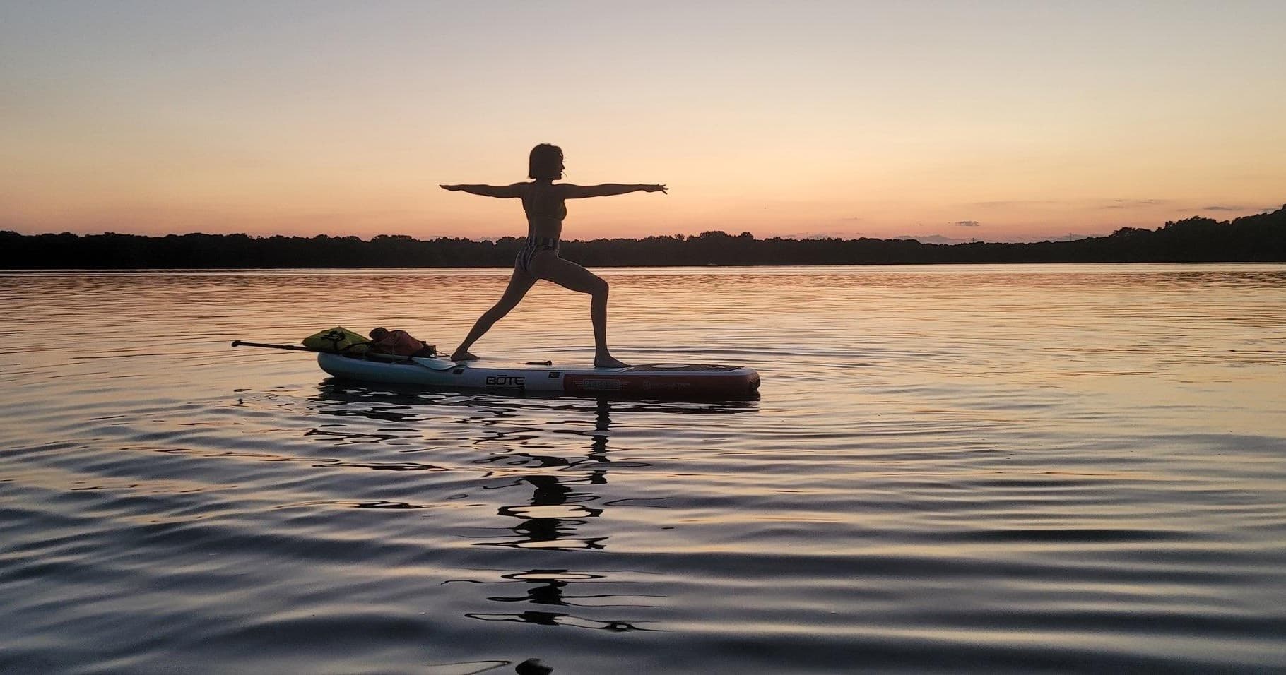 Sunset paddleboard yoga silhouette practicing warrior pose on lake