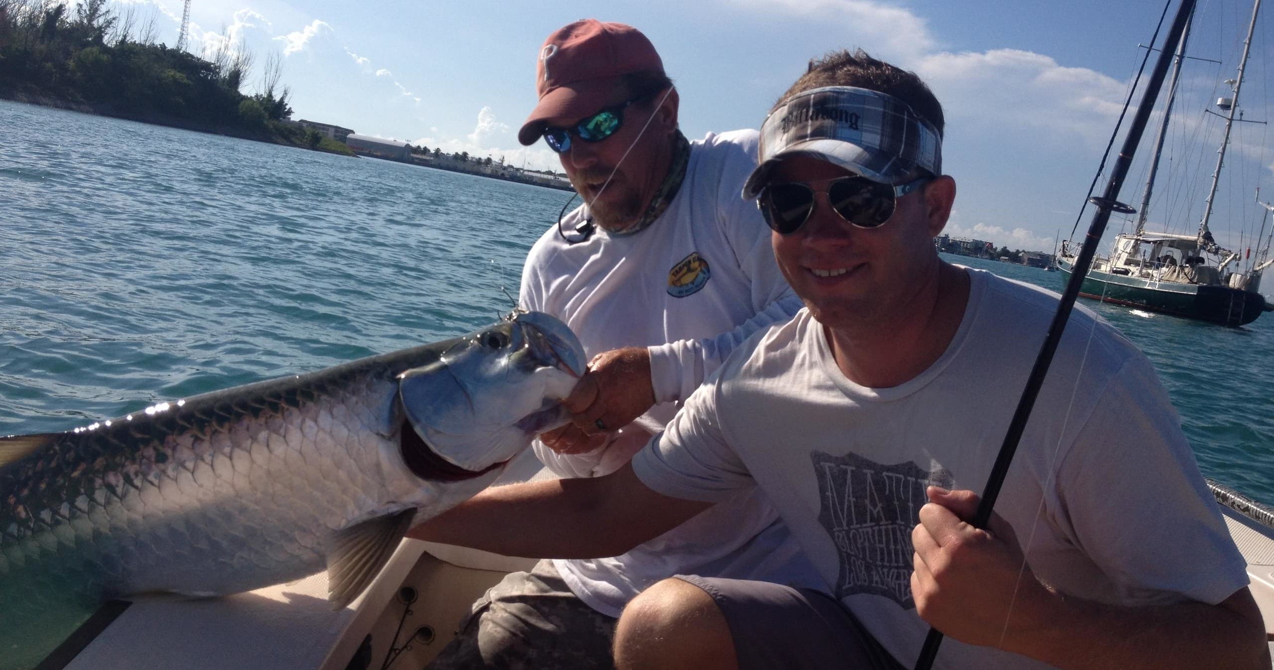 Fishermen posing with tarpon on sunlit flats near shore