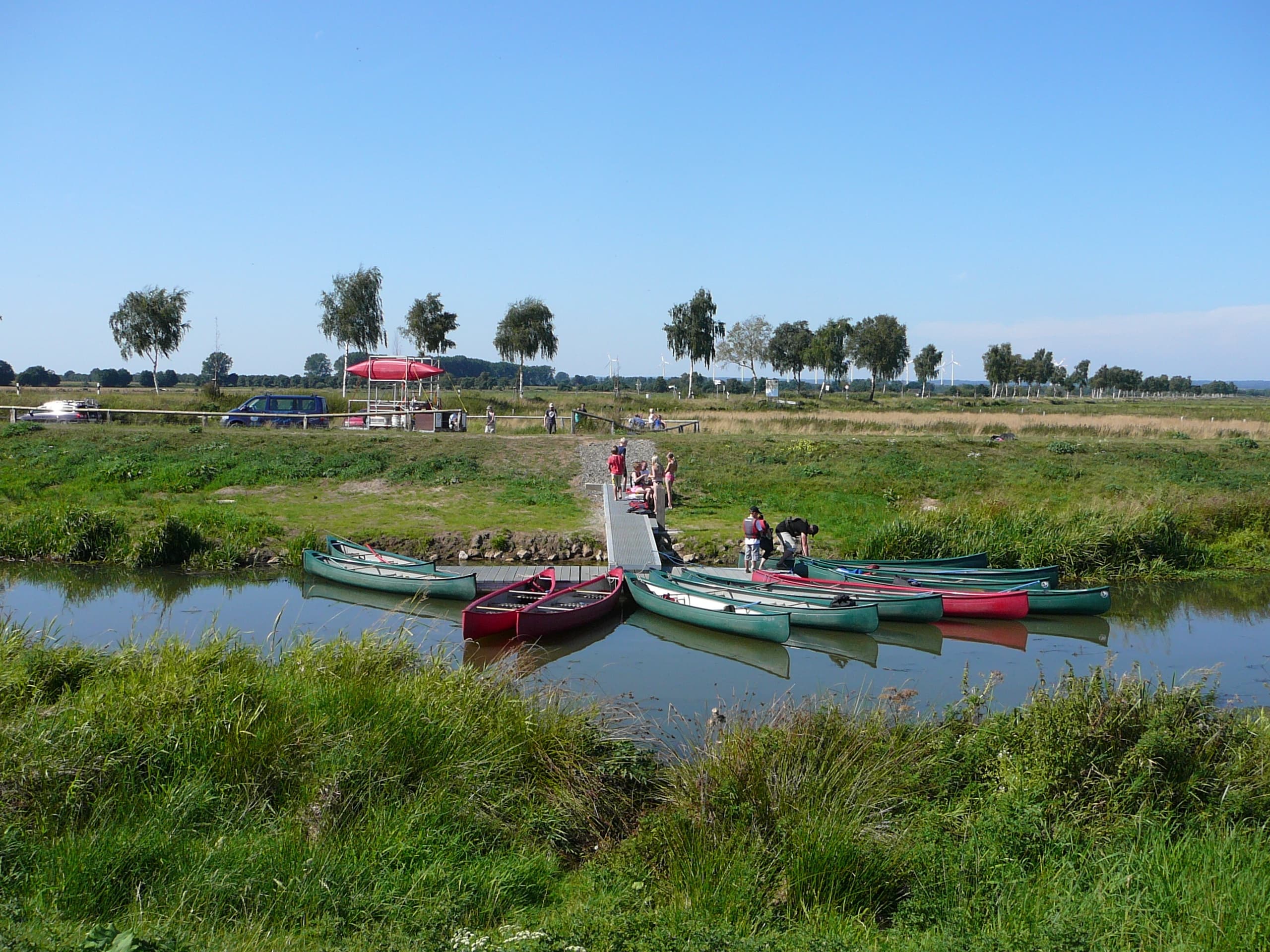 Canoes moored at a grassy river dock on calm countryside water