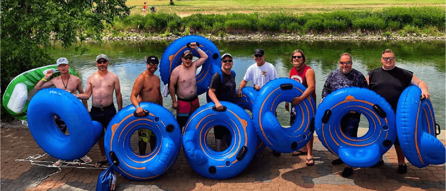 Group river tubing on grassy riverbank with blue inner tubes