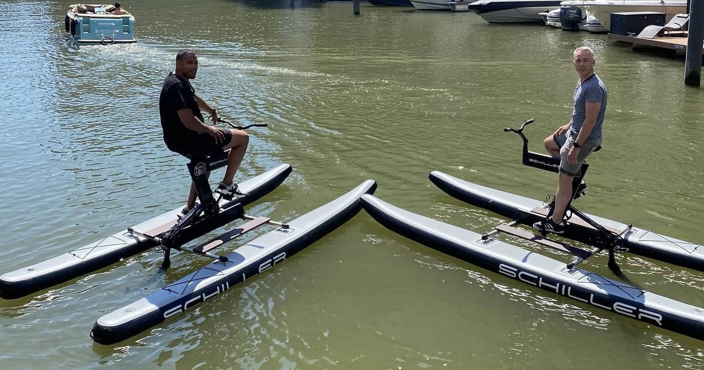 Two riders on hydrofoil water bikes in sunny urban marina
