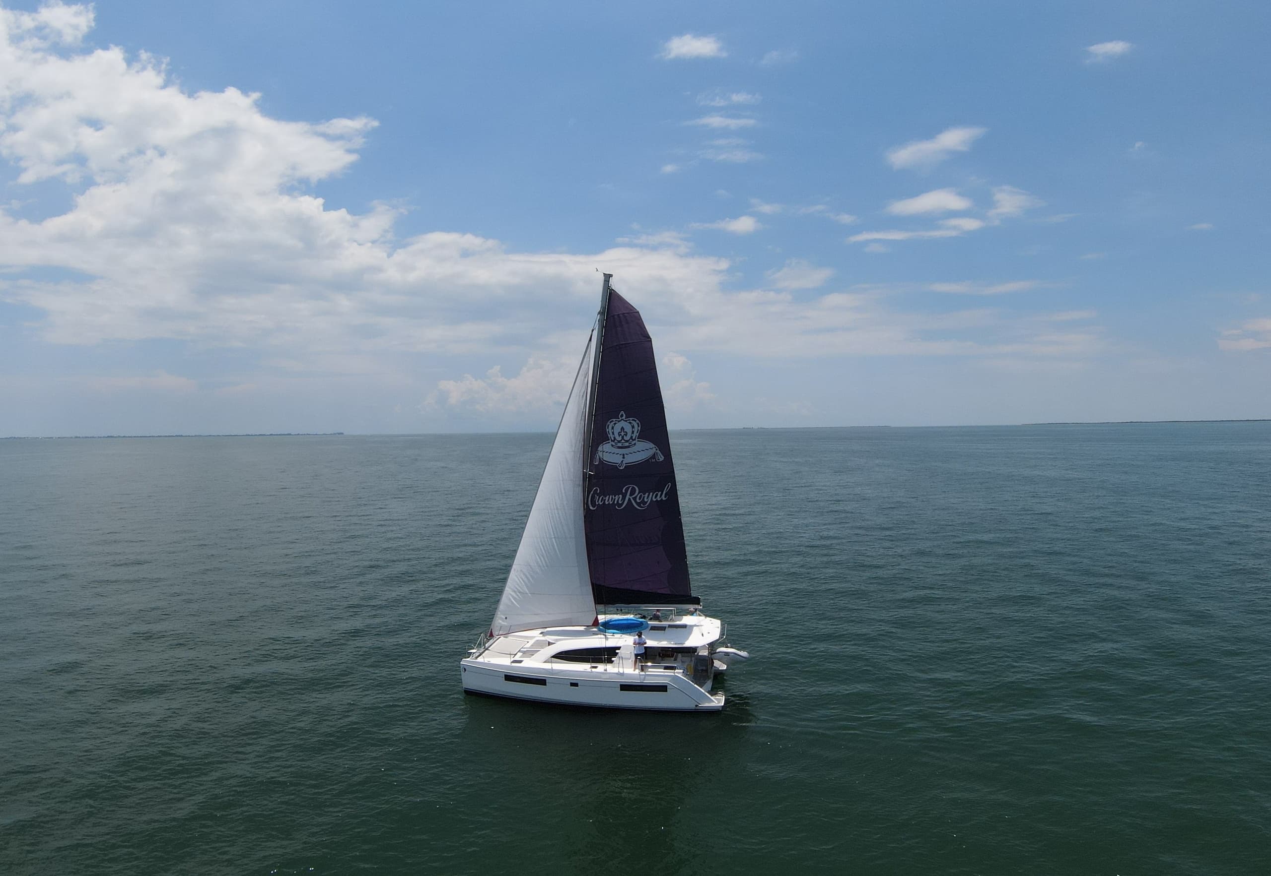 Catamaran sailing on open sea under blue sky, aerial view